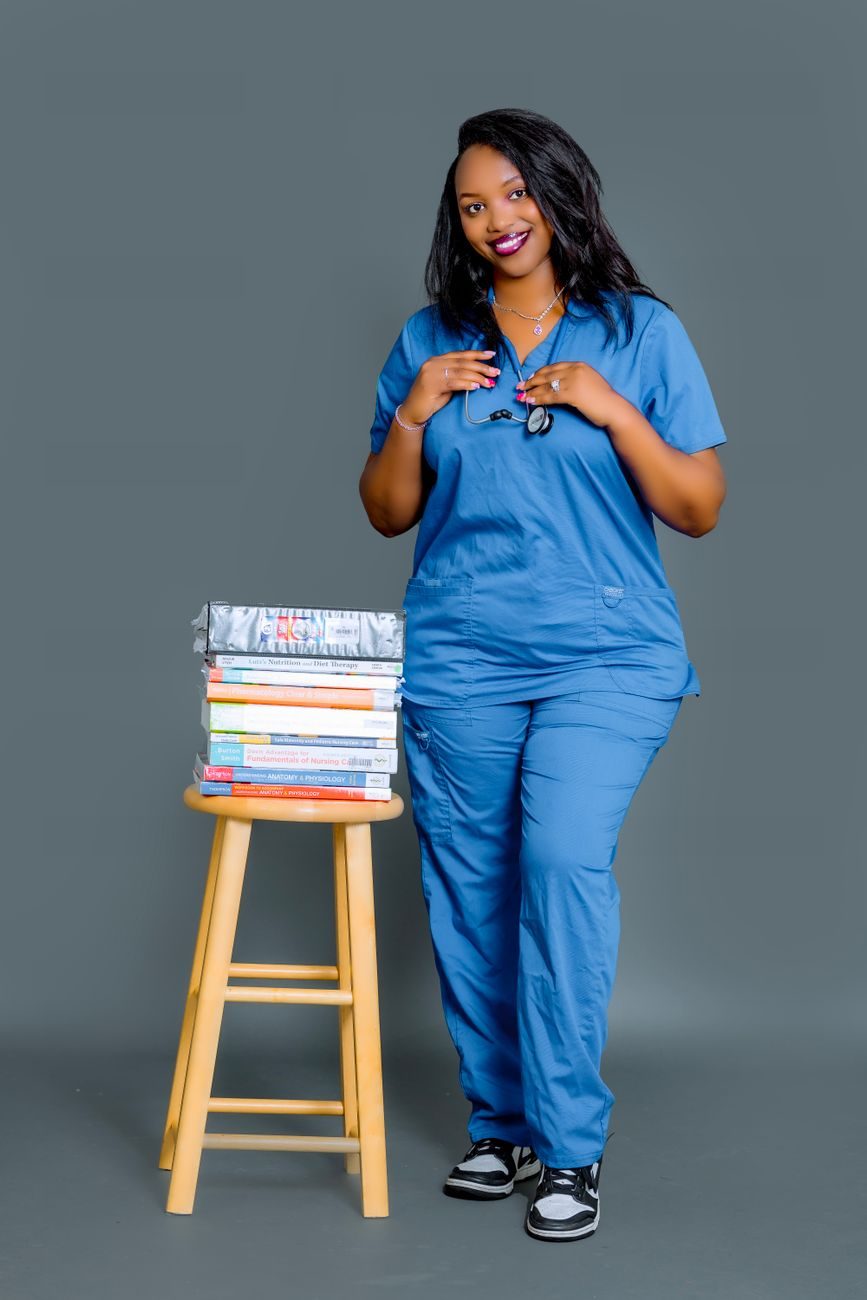 A smiling nurse in blue scrubs with a stethoscope beside her nursing textbooks